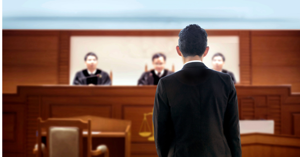 Man standing in a courtroom facing a panel, highlighting a legal proceeding