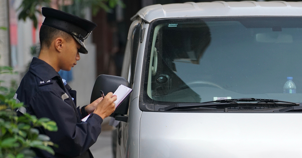 Police officer writing a ticket next to a vehicle, representing traffic law enforcement