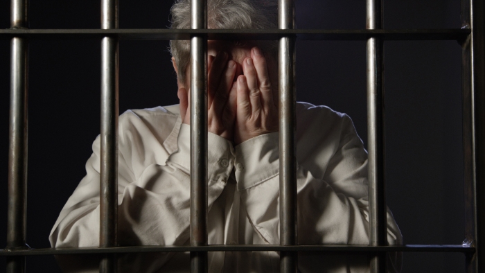 Elderly woman in Dark Prison behind bars of the jail