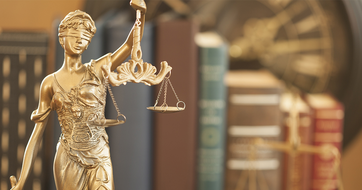 Golden statue of Lady Justice holding scales, with books and a clock in the background